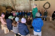 Kinder sitzen im Kreis und hören einer Frau zu, die in der Mitte des Kreises steht und erzählt.