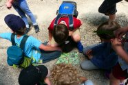 Kinder hocken im Kreis auf einem Schotterweg und haben in der Mitte eine Schatzkarte